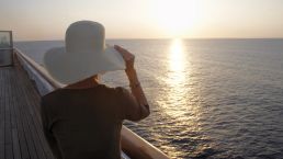 Dame mit Hut genießt vom Schiff aus den Sonnenuntergang
